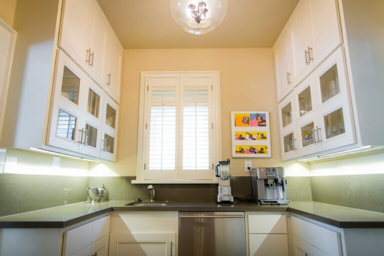 Modern kitchen with white cabinets, a window, coffee machines, and colorful art on the wall.