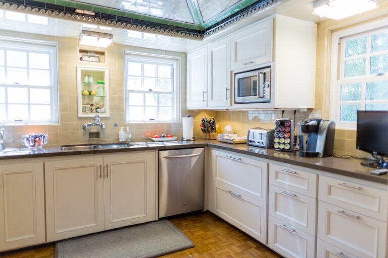 Modern kitchen with white cabinets, stainless appliances, coffee maker, and windows letting in natural light.