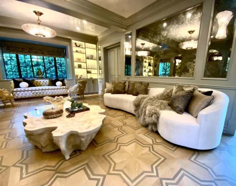 Elegant living room with a curved white sofa, fur throw, geometric rug, sculpted coffee table, and large mirrored wall.