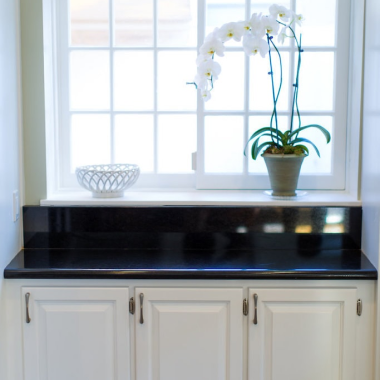 White cabinets with a black countertop and a potted orchid show off a stunning cabinet refresh by the large window.