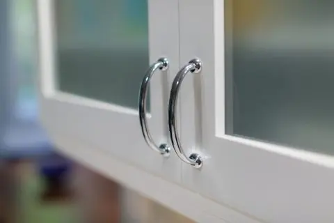 Close-up of two chrome cabinet handles on white doors with frosted glass panels in Los Angeles.