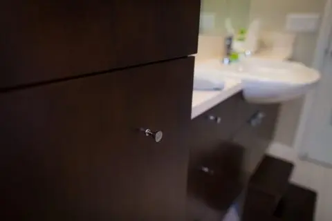 A bathroom cabinet drawer is slightly open with a screw poking out where a handle should be.