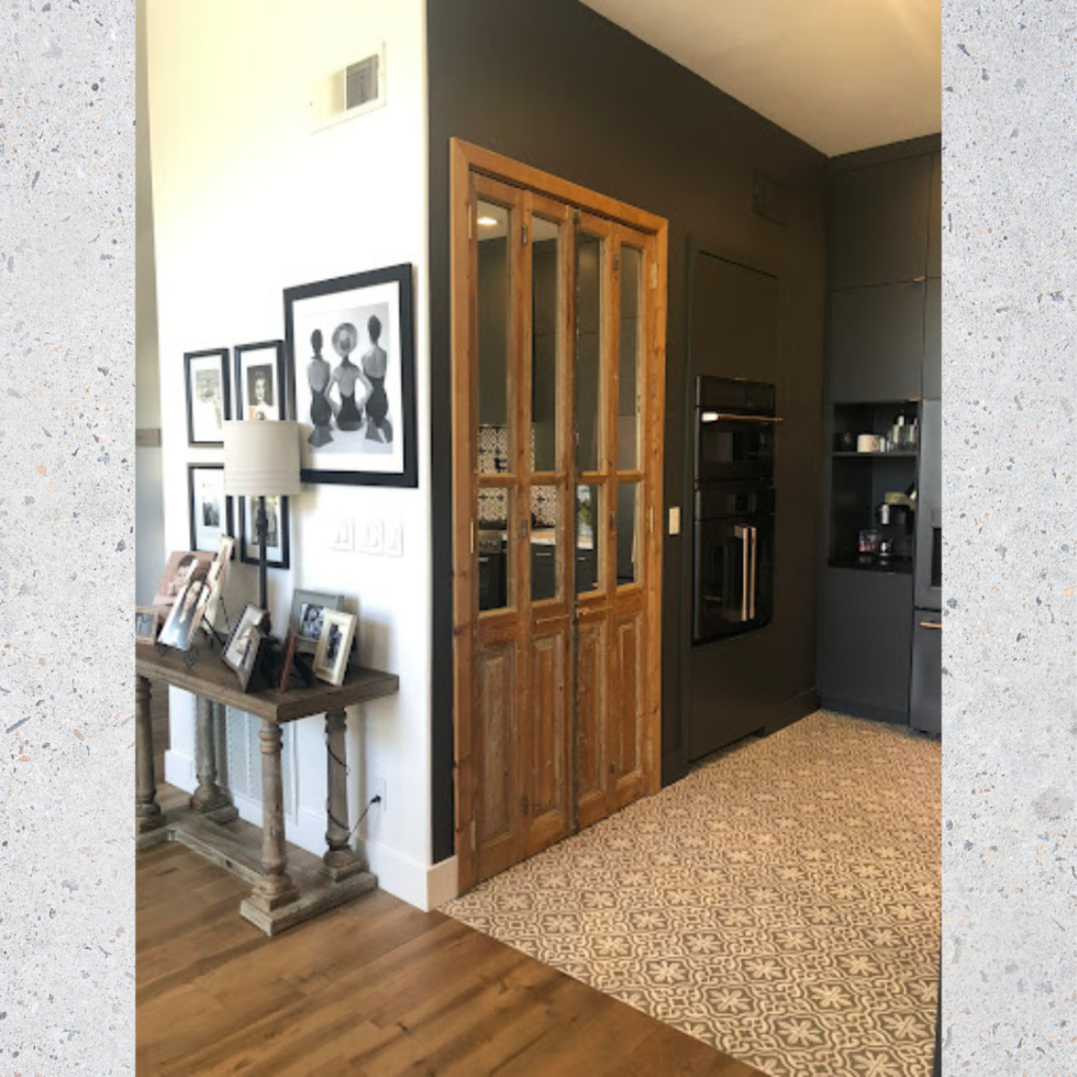 A modern room with patterned tile floor, wooden double doors, wall art, and a console table with framed photos.