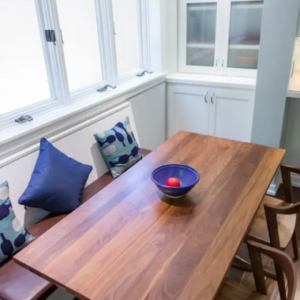 Wooden dining table with a blue bowl and red apple, surrounded by chairs and a bench with patterned cushions.