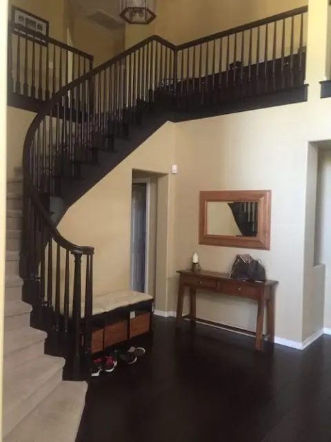 Modern entryway with a dark wood staircase, hallway table, wall mirror, storage bench, and shoes on a dark floor.
