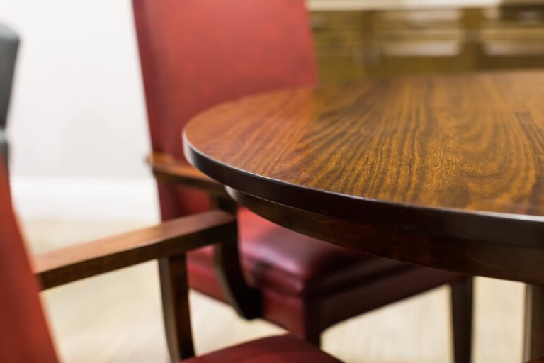 Close-up of a round wooden table with red upholstered chairs in a softly lit room.