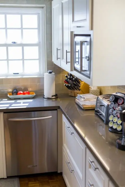 Modern kitchen with gray countertops, white cabinets, a dishwasher, knife block, toaster, and coffee pod holder.