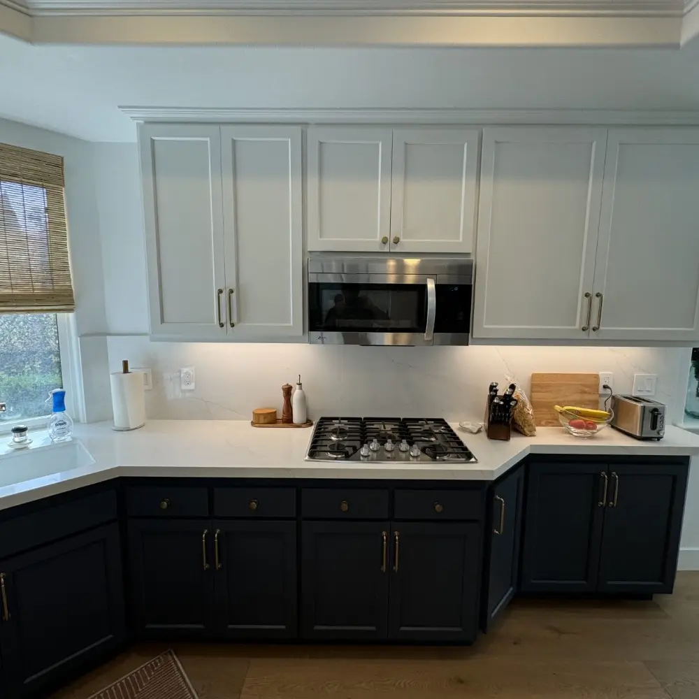 Modern kitchen with white uppers, dark stain lower cabinets, gas stove, microwave, and countertop appliances.