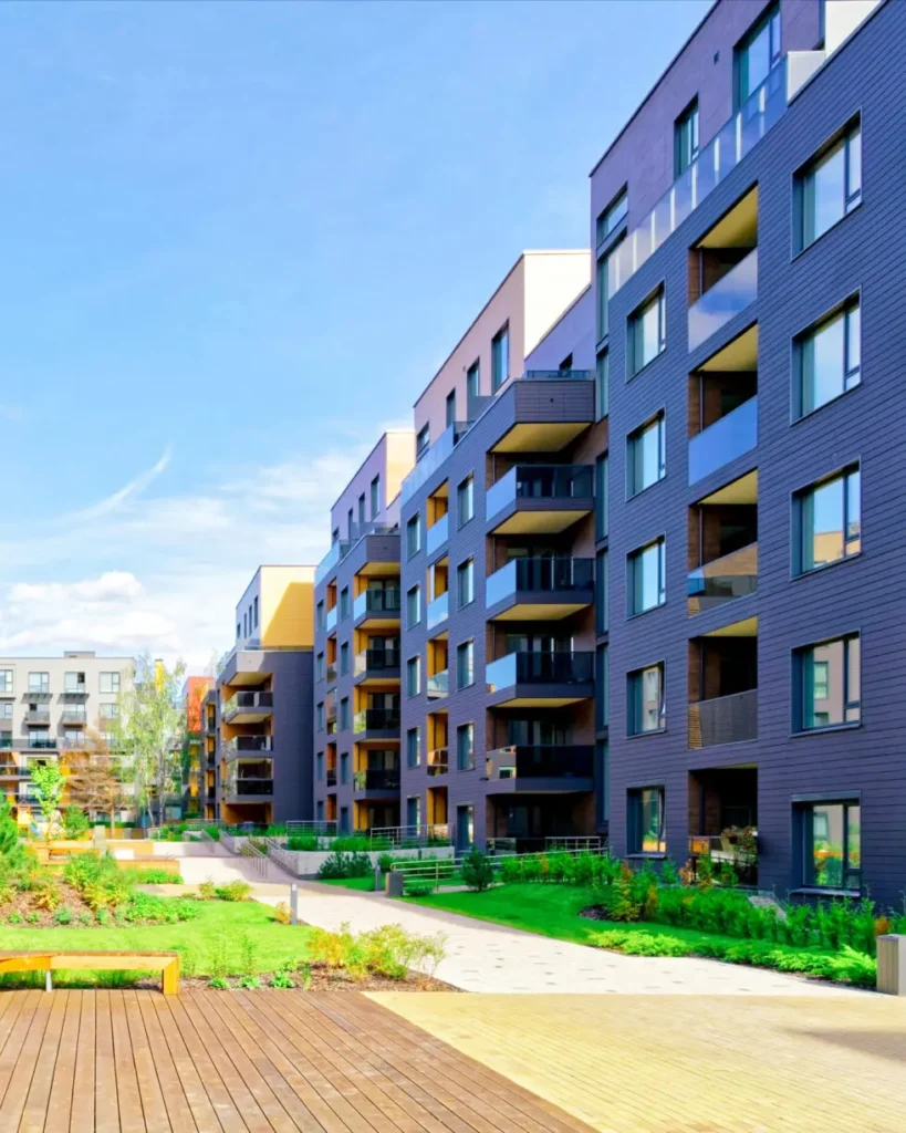 Modern apartment buildings with balconies overlooking a landscaped courtyard and wooden walkway on a sunny day.