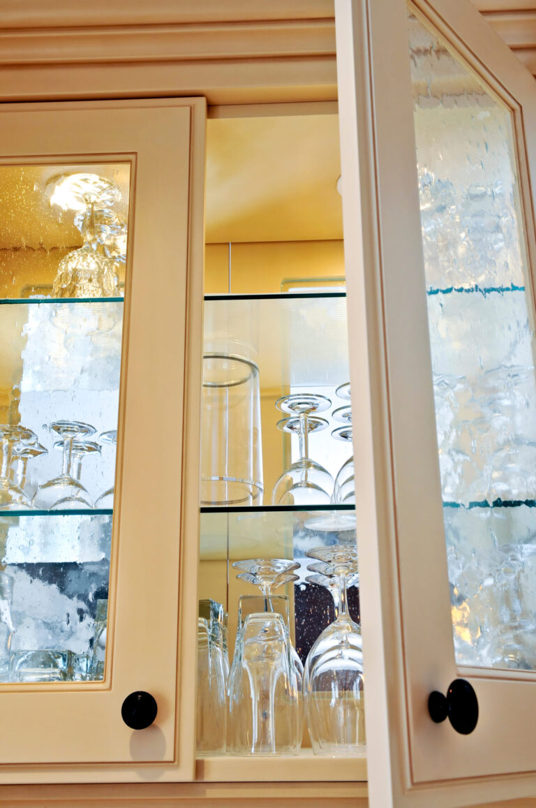 Glass cabinet with glass doors, displaying various glasses neatly arranged on glass shelves inside.