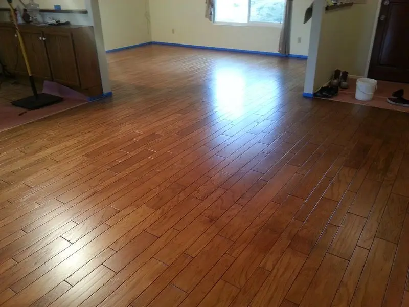 Empty room with shiny, newly installed wooden floor and sunlight streaming in through a window.