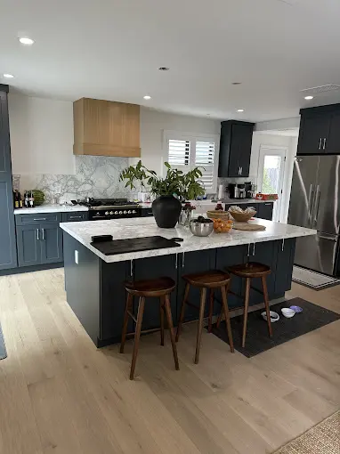 Modern kitchen with dark cabinets, marble countertops, island seating, and stainless steel appliances. Plant on island.