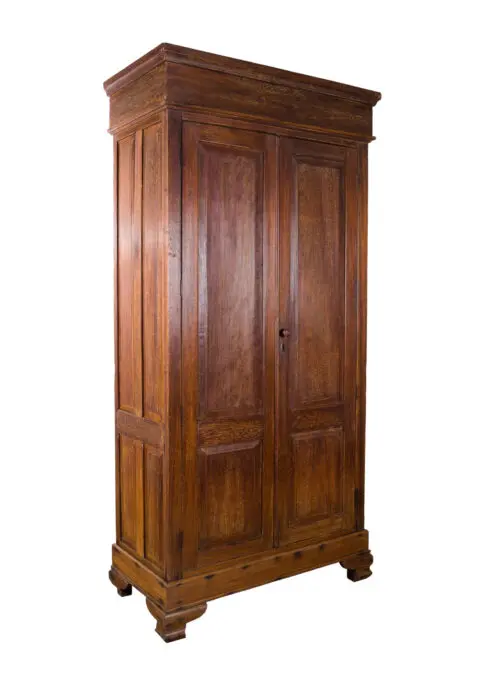 A tall, vintage wooden wardrobe with two paneled doors, standing on four short, carved feet. The wardrobe has a classic, rectangular design with a slightly protruding top section.