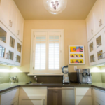 Bright Los Angeles kitchen with white cabinets, two coffee machines, wall art, and window shutters above the sink.
