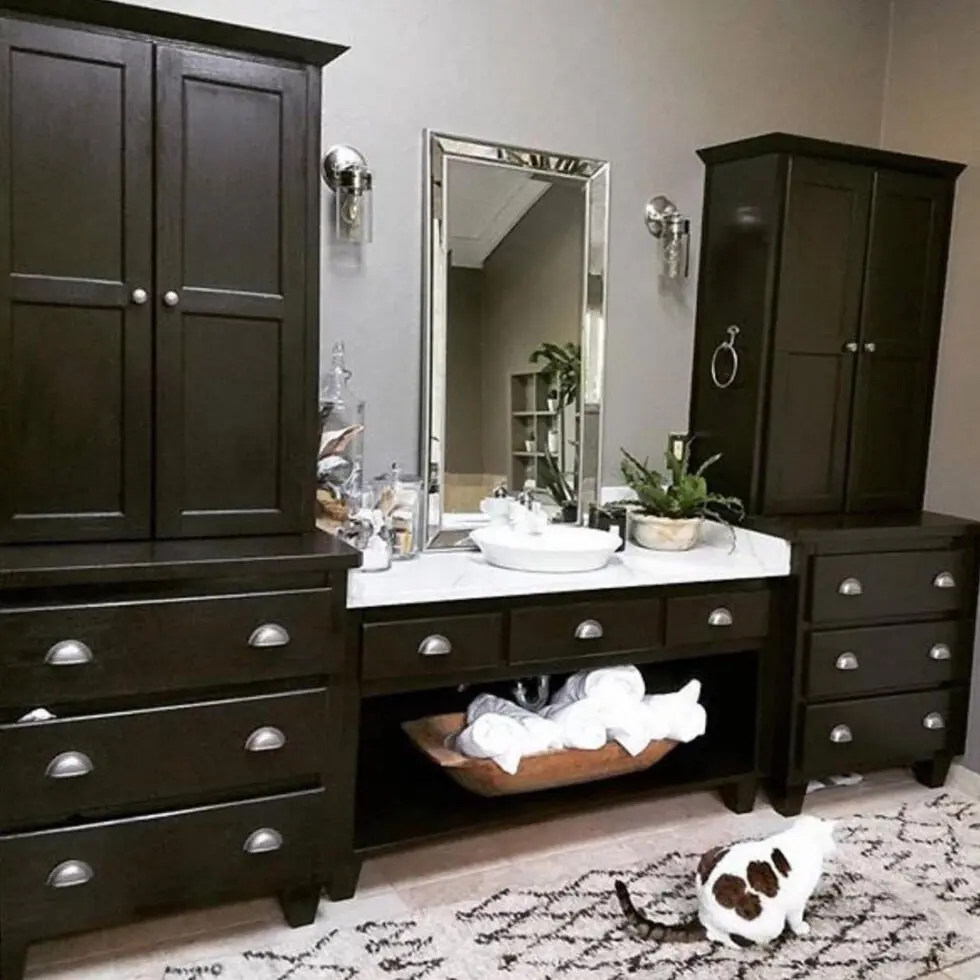 Dark wood bathroom vanity with a mirror, sink, towel shelf, and a cat on a patterned rug in front.