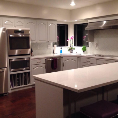 Modern kitchen with a cabinet refresh—white cabinets, stainless steel appliances, and a large white countertop island.
