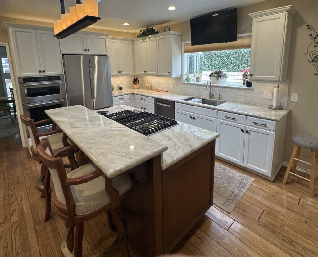 Modern kitchen with white cabinets, marble island, gas stove, wooden floor, and cushioned bar stools.