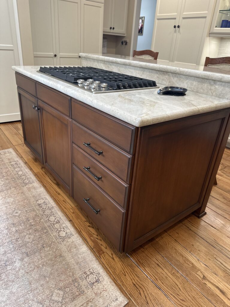 Wood kitchen island with drawers, marble countertop, built-in gas cooktop, and wooden floor.