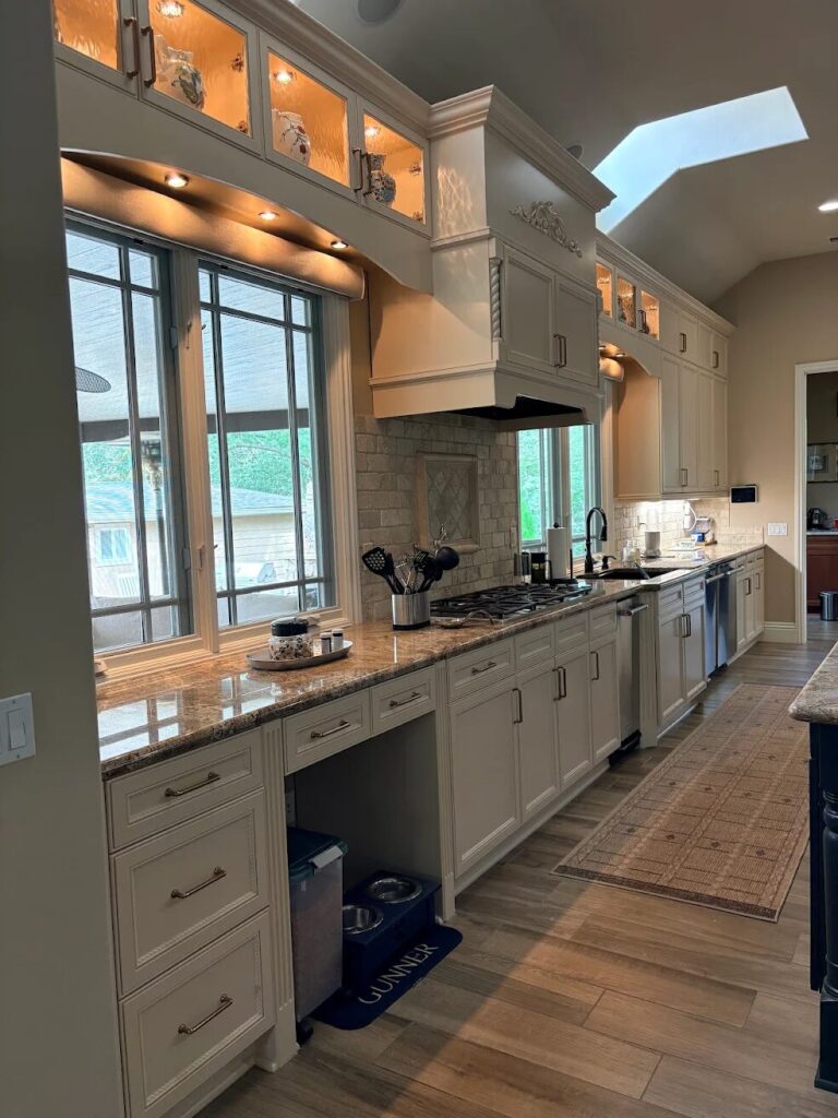 Spacious white kitchen with custom cabinets, granite countertops, a skylight, and a large window.