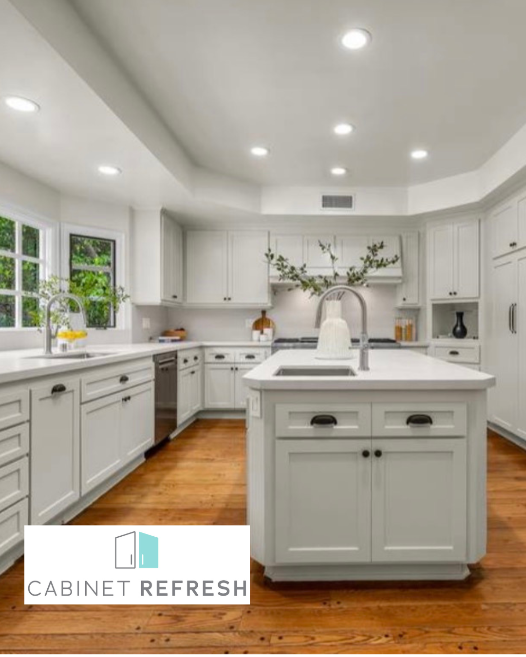 Bright kitchen featuring white shaker-style cabinets, a matching central island, white countertops, stainless steel appliances, and warm hardwood flooring. The refreshed cabinetry creates a clean, timeless look.